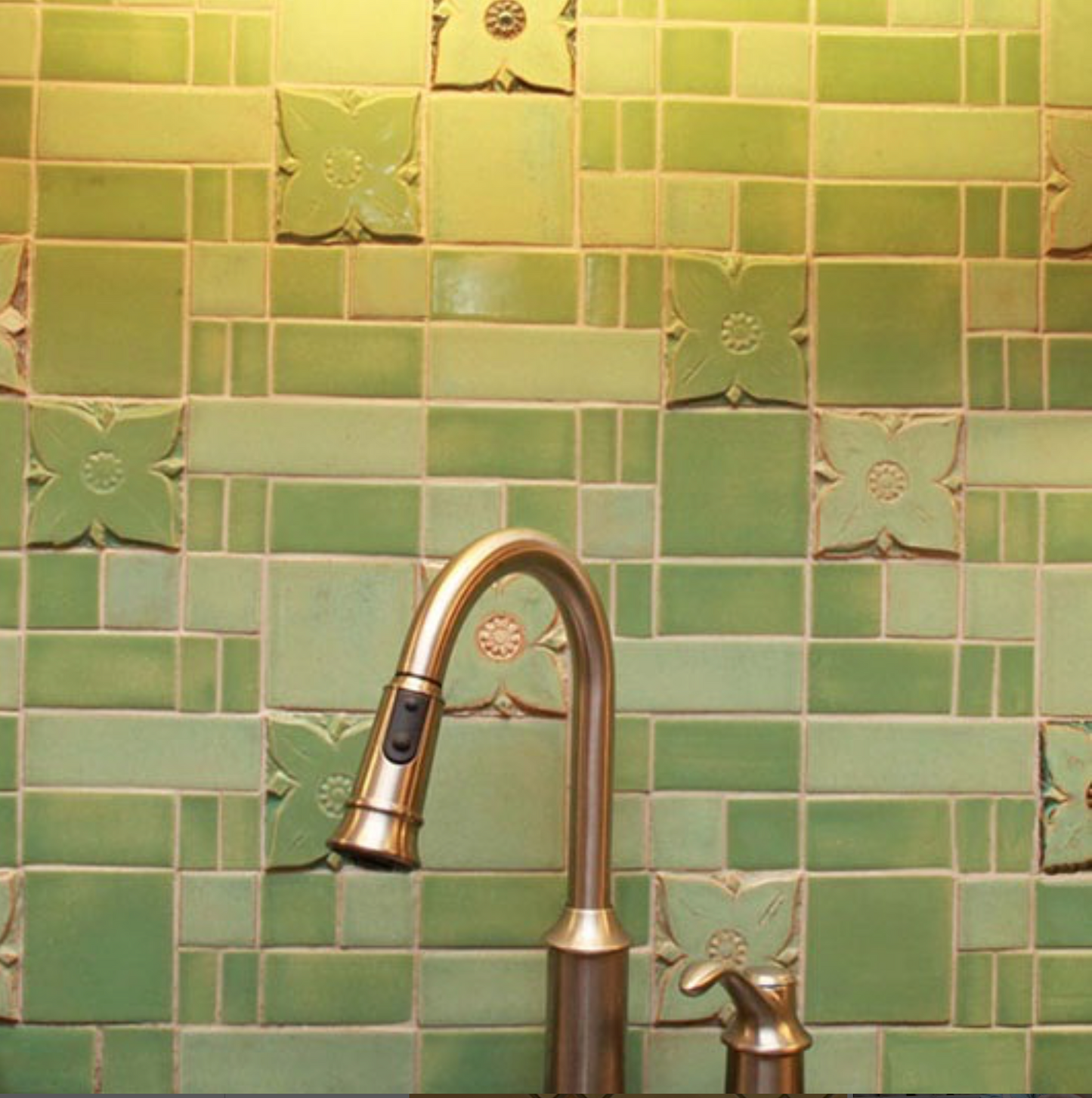 Green ceramic tiles with a floral pattern installed on a kitchen wall, featuring a silver faucet.