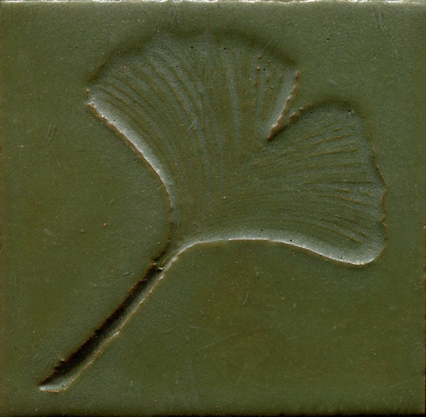 A green ceramic tile with a stamped leaf design.