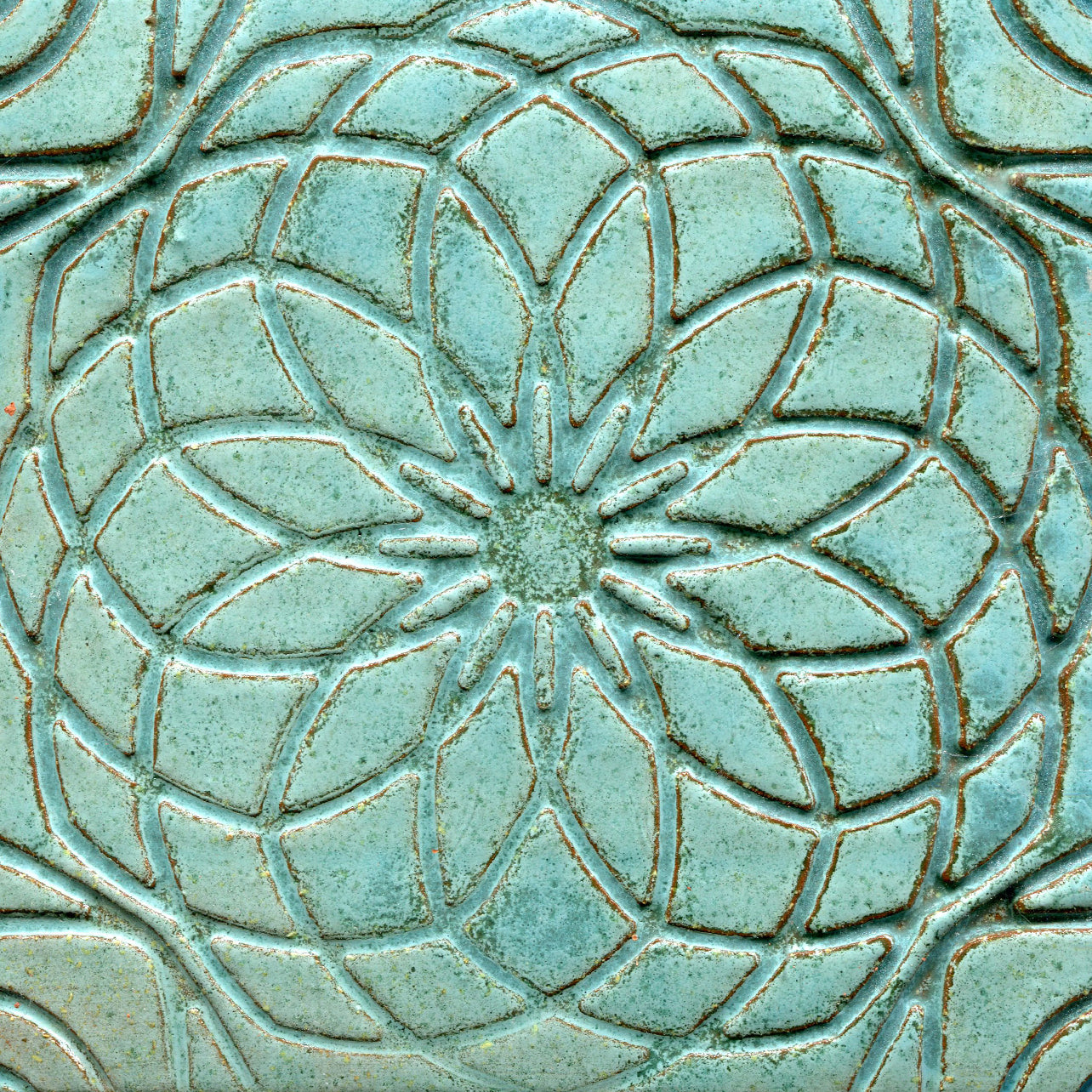 Turquoise green stamped tile with a geometric floral pattern.