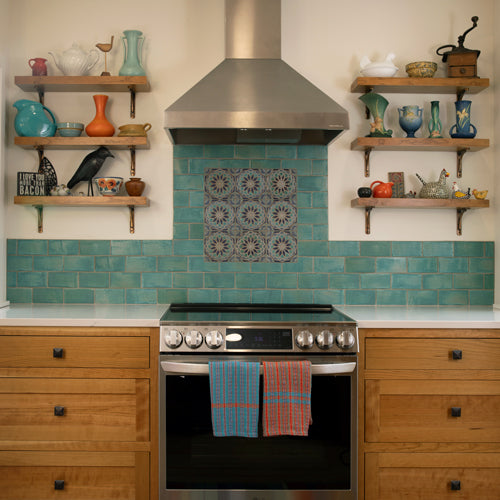 Kitchen with teal tiled backsplash, wooden shelves, and stainless steel oven.