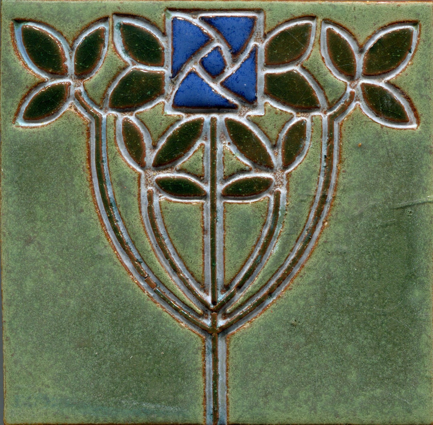 A stamped tile featuring a floral Art Nouveau design with intertwined stems and vibrant, multicolored petals on a green background.
