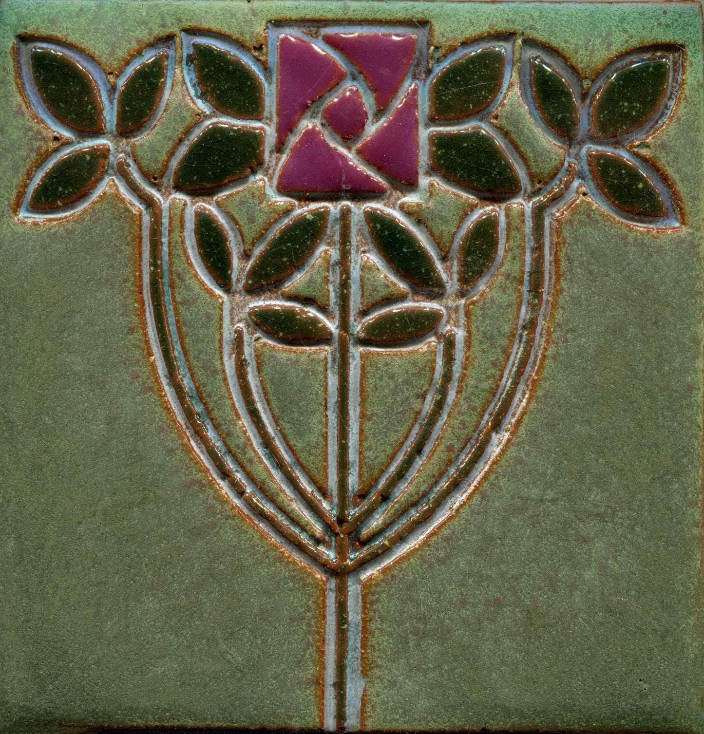 A stamped tile featuring a floral Art Nouveau design with intertwined stems and vibrant, multicolored petals on a green background.