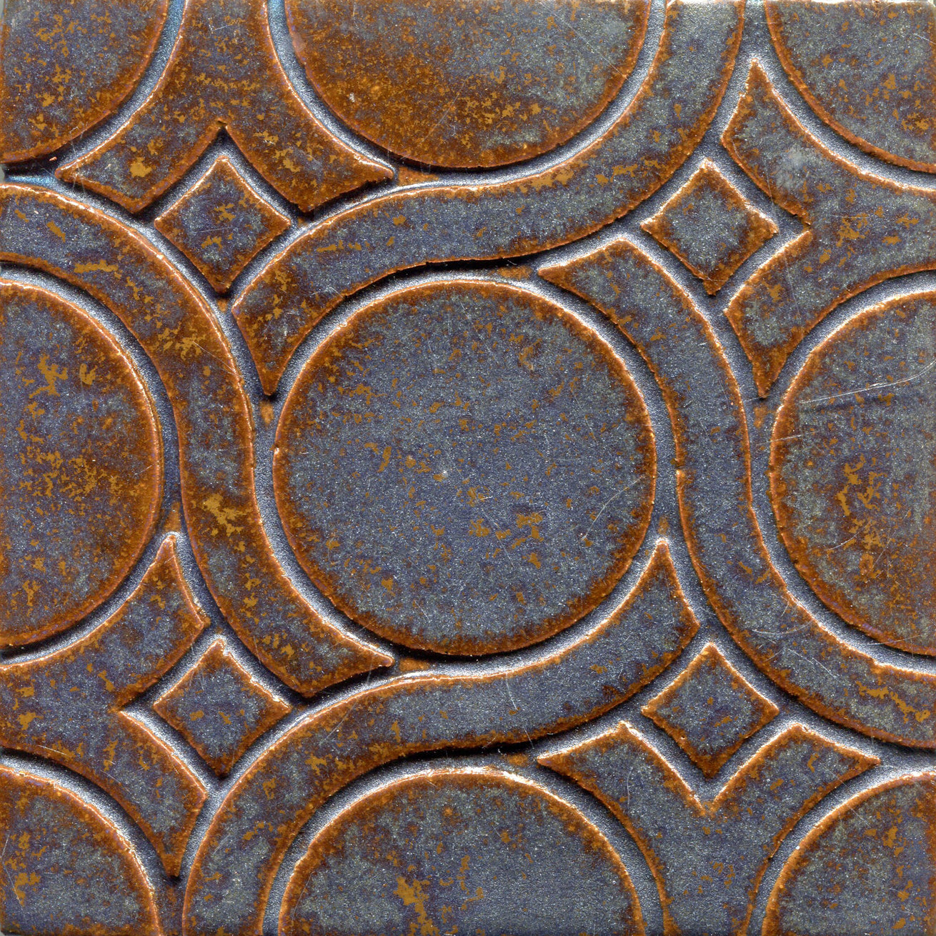 A pattern of woven knots on stamped tiles, copper and blue colors creating a geometric design.