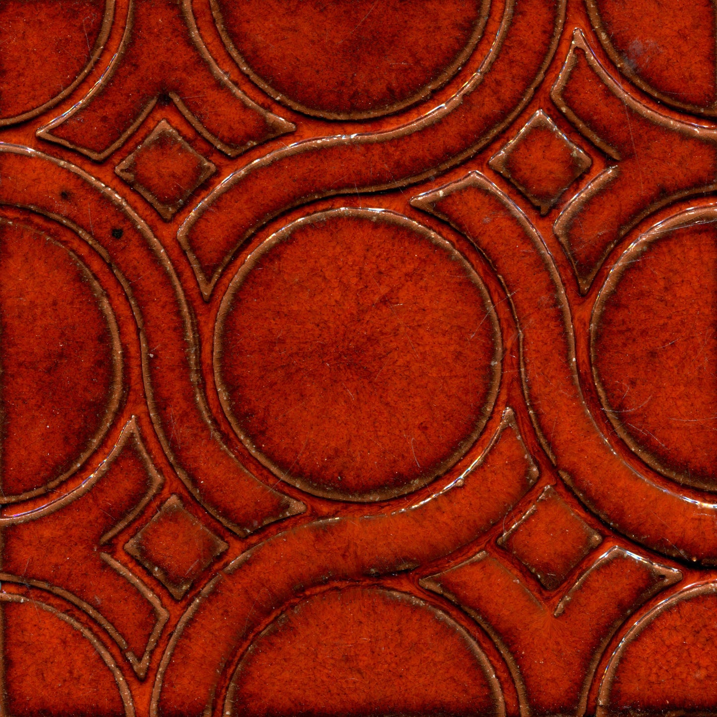 A pattern of woven knots on stamped tiles, with orange colorscreating a geometric design.