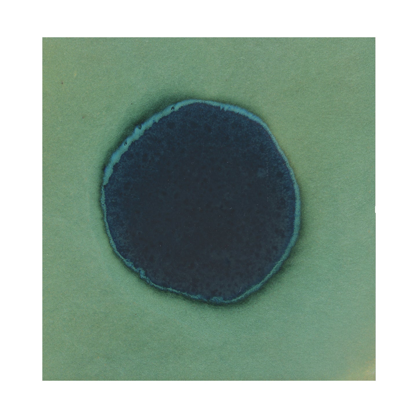 A close-up image of a surface with a dark blue spot in the center, transitioning from a dark blue to an Avocado green color around the edge.