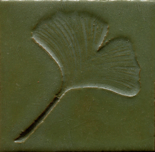 A green ceramic tile with a stamped leaf design.