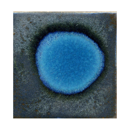 A ceramic artwork with a blue metallic spot and a surrounding darker blue texture on a darker background.