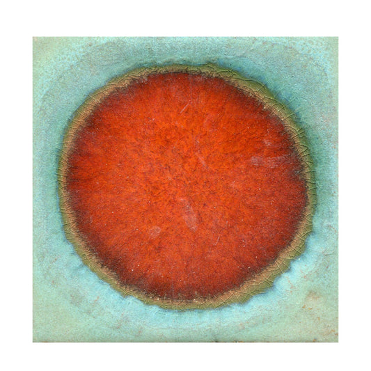A ceramic plate with a central vibrant red spot surrounded by a copper patina finish, with a green border.